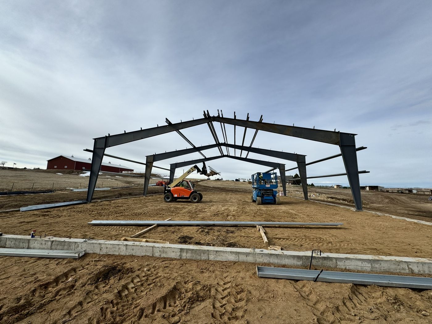 Steel building frame going up on a job site, with a telehandler and scissor lift